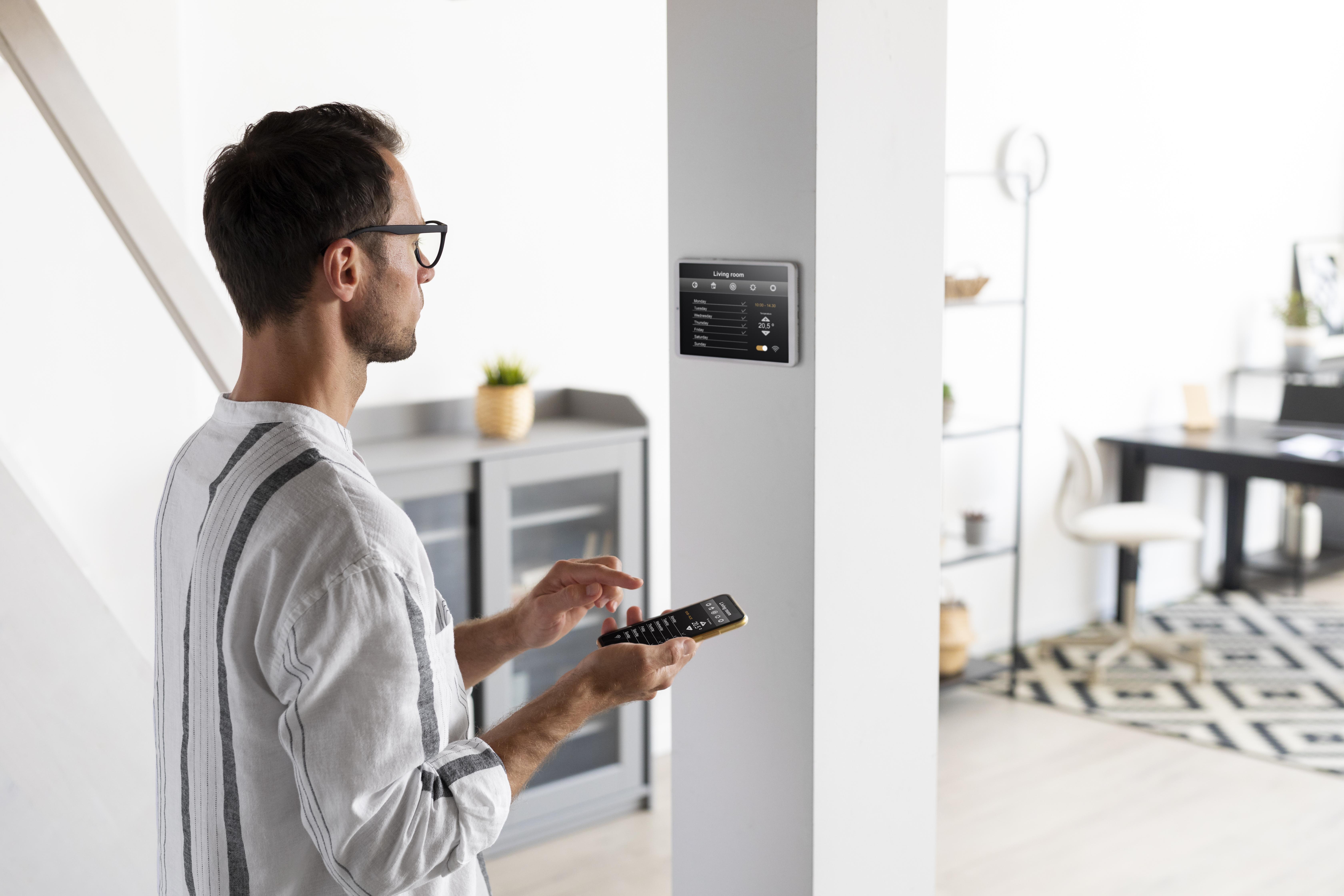 Man adjusting devices with phone and wall display